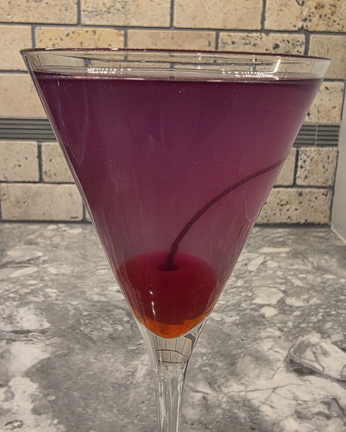 Close-up of the Aviation cocktail showing the purple-to-cherry-red color gradient created by the maraschino cherry garnish bleeding into the drink