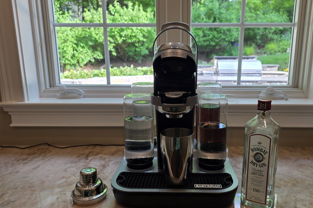 The Bartesian machine dispensing the Bee's Knees base into a stainless steel shaker, with a bottle of Bombay London Dry gin alongside