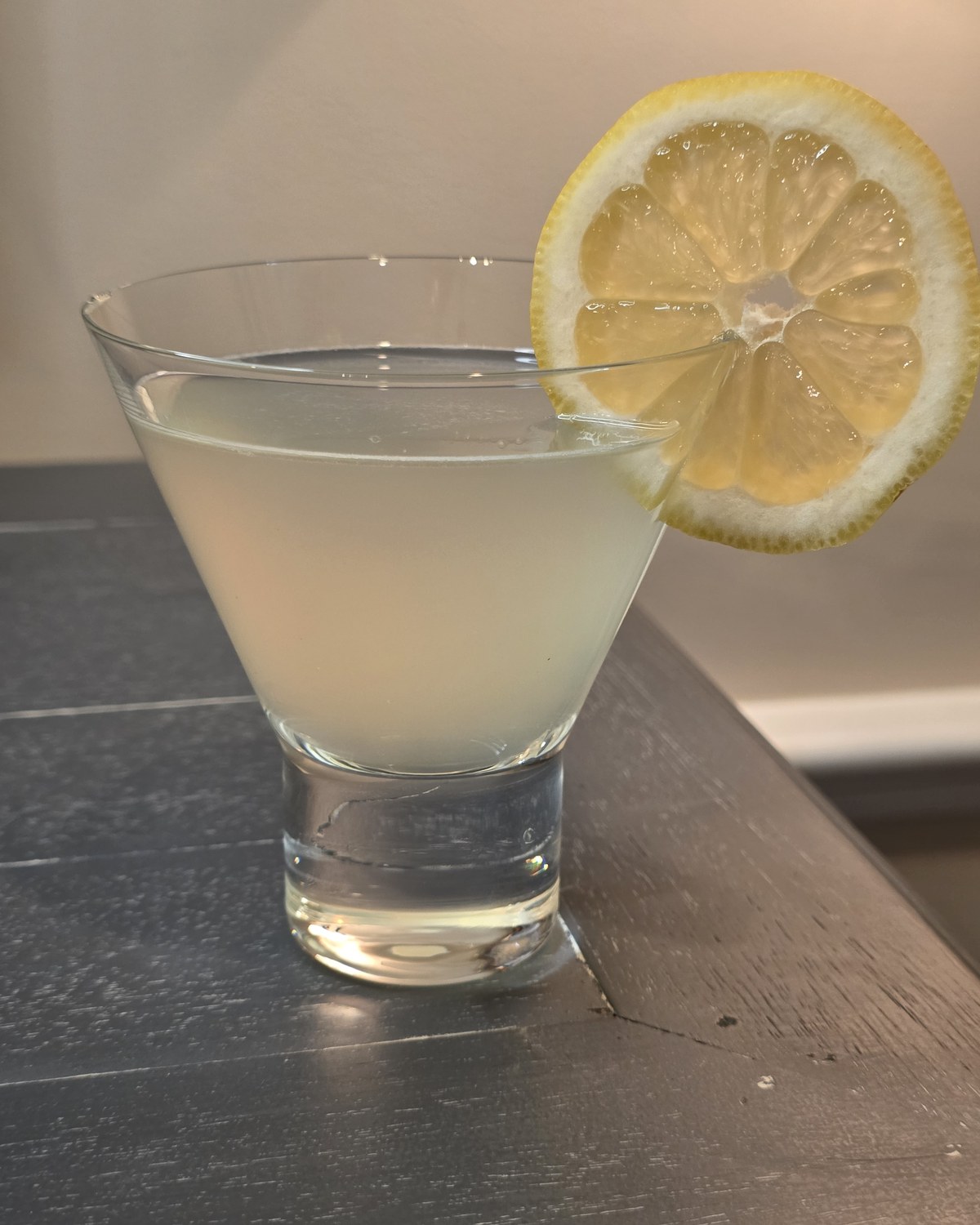 Bartesian Lemon Drop cocktail in a stemless martini glass with a lemon wheel, hazy pale yellow, on a home bar