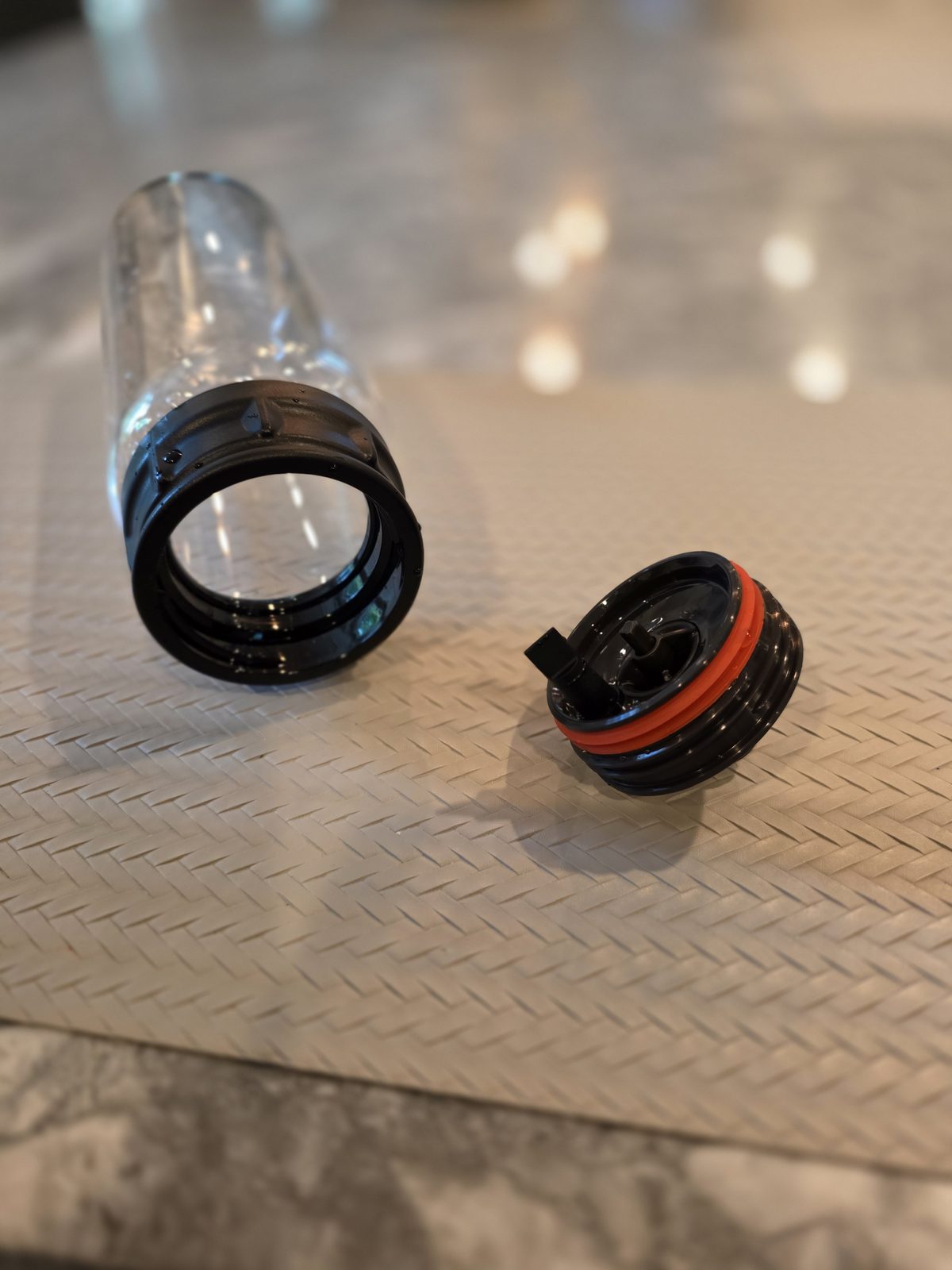 A Bartesian Premier spirit bottle taken apart, showing the permanent plastic collar on the glass, the dispenser cap, the red O-ring washer, and the small rubber valve