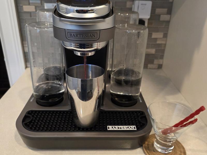The Bartesian Premier pouring a red Vampire's Kiss into a stainless steel shaker, with a stemless martini glass holding two red licorice twists beside it