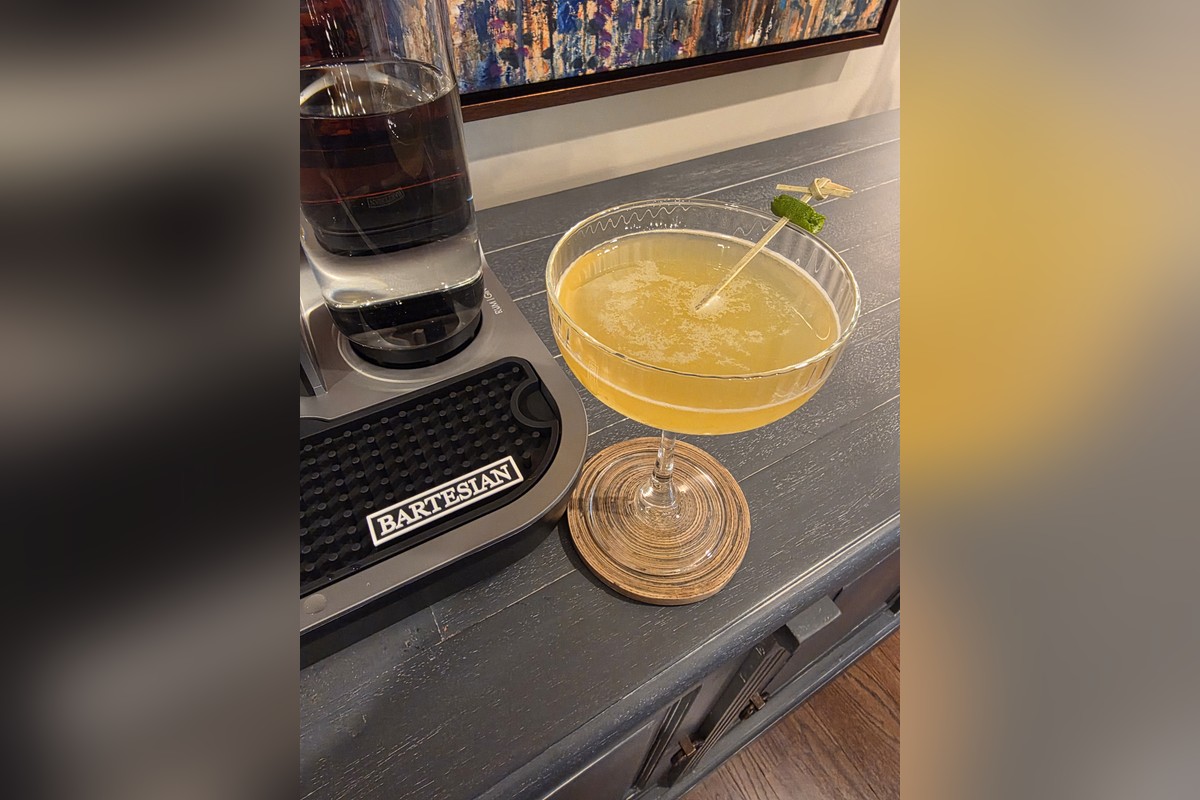 Finished Calamansi Daiquiri cocktail in a coupe glass with green lime garnish, alongside the Bartesian machine on a home bar