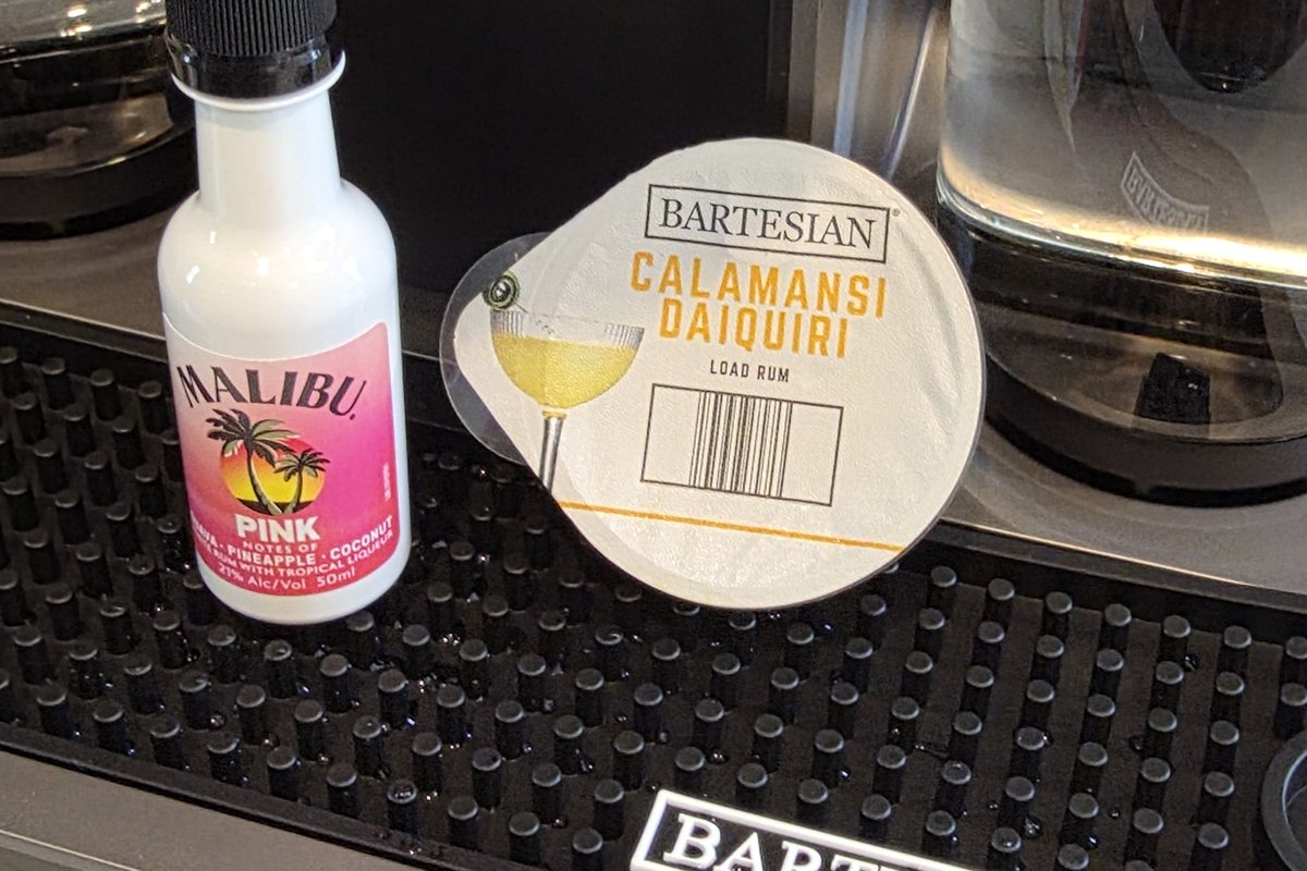 A Malibu Pink coconut rum mini bottle beside a Bartesian Calamansi Daiquiri pod on the machine drip tray