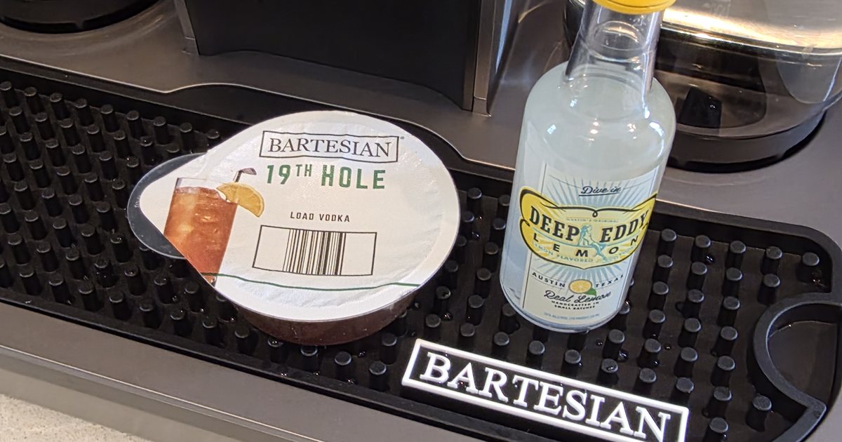 A Deep Eddy Lemon flavored vodka mini bottle beside a Bartesian 19th Hole pod on the machine drip tray