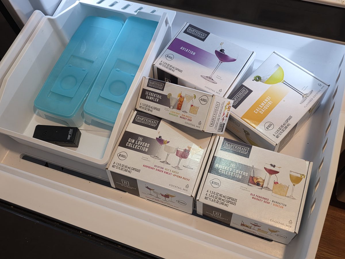 Bartesian cocktail pod boxes stored in a freezer drawer beside blue ice packs, which holds their presentation for up to twelve months.