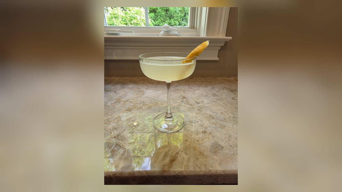 A pale gold Bee's Knees gin cocktail with a lemon twist in a coupe by a bright window.