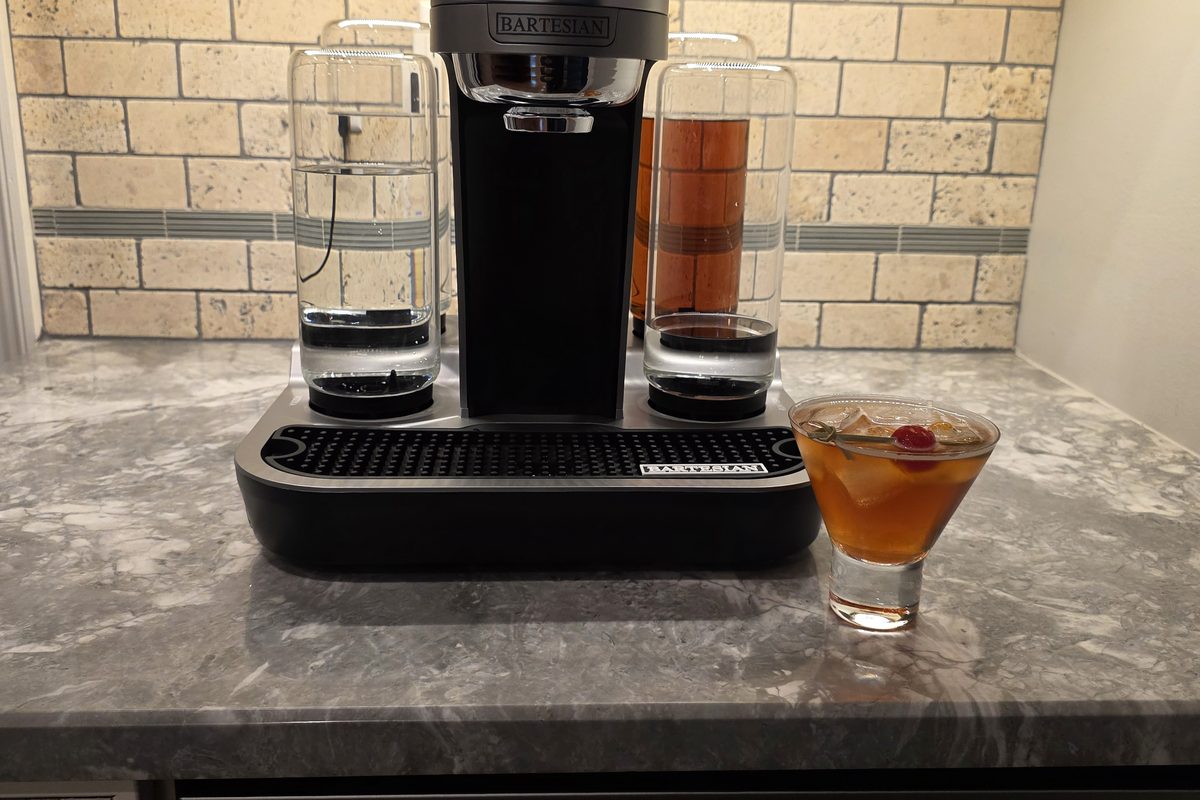A finished Bartesian Manhattan over ice with a cherry, next to the Bartesian machine on a marble counter