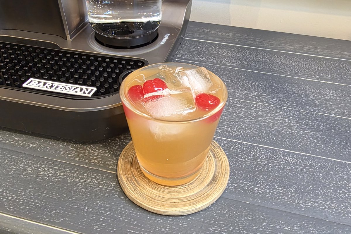 Finished Bartesian Whiskey Sour in a low ball glass with maraschino cherries and ice, beside the Bartesian machine on a home bar